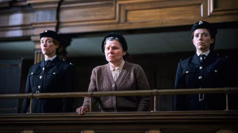 Vera Drake (Imelda Staunton) stands between two police officers in a courtroom
