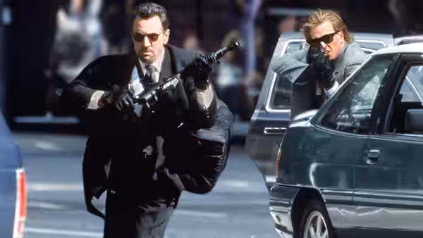 Lt. Vincent Hanna (Al Pacino) aiming a submachine gun beside a car