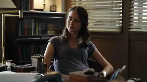 Iris Campbell (Wrenn Schmidt) seated at a desk in an office