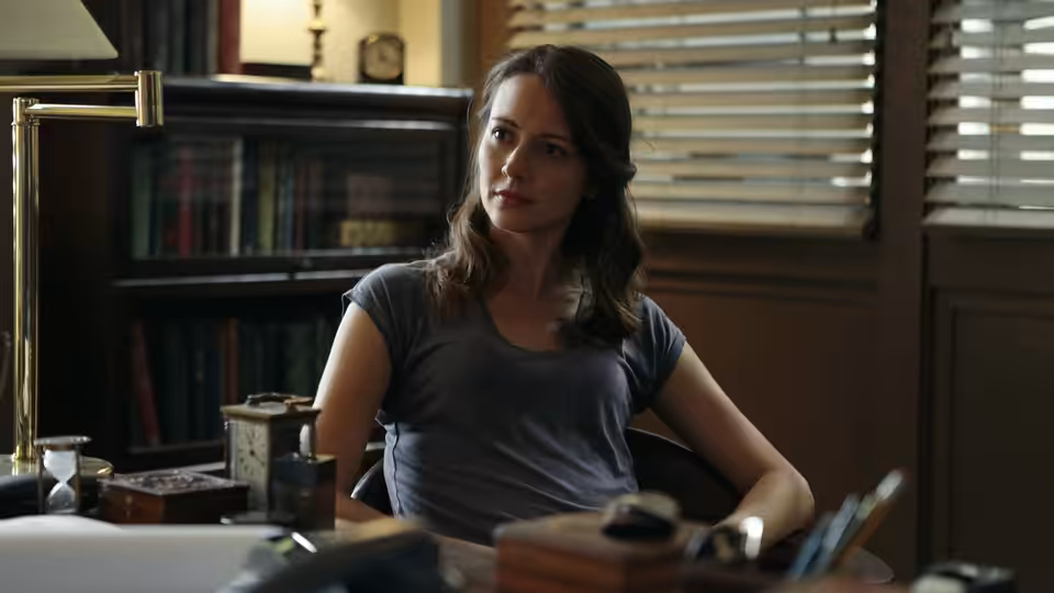 Iris Campbell (Wrenn Schmidt) seated at a desk in an office