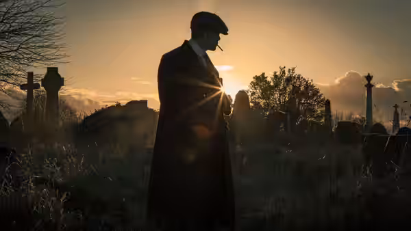 Thomas Shelby standing in a grassy graveyard at sunset