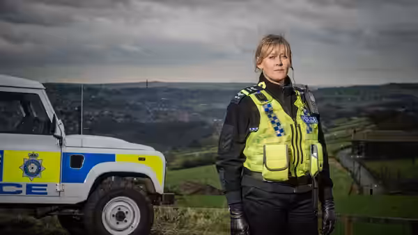 Catherine Cawood (Sarah Lancashire) stands beside a police vehicle in hilly countryside
