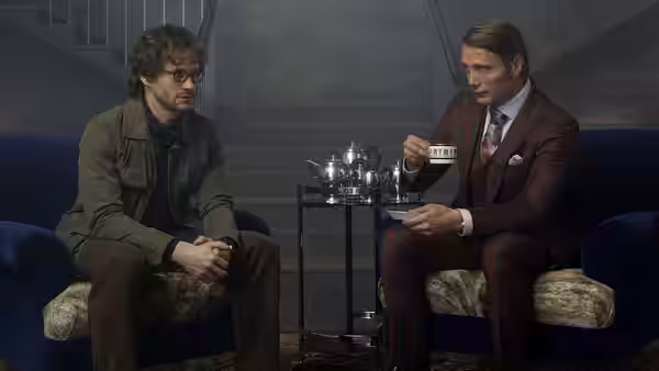 Dr. Hannibal Lecter (Mads Mikkelsen) sipping tea opposite Will Graham (Hugh Dancy)