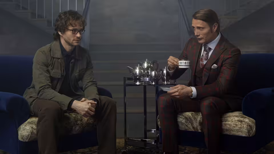 Dr. Hannibal Lecter (Mads Mikkelsen) sipping tea opposite Will Graham (Hugh Dancy)