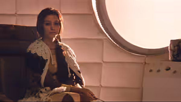 a woman with braided hair sits in a chair beside a round window