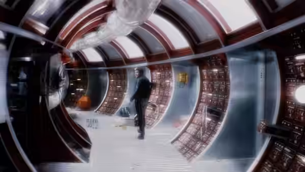 a man stands alone in a curved corridor lined with control panels