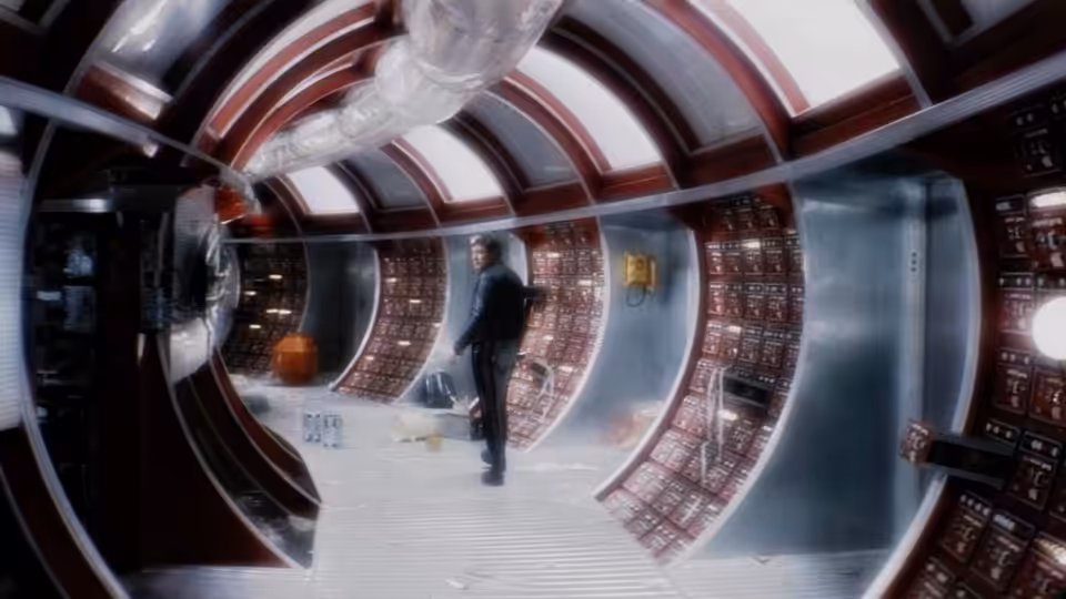 a man stands alone in a curved corridor lined with control panels
