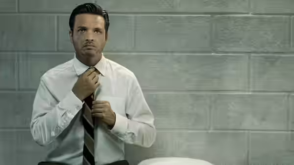 Man in a white shirt adjusts his tie against a brick wall