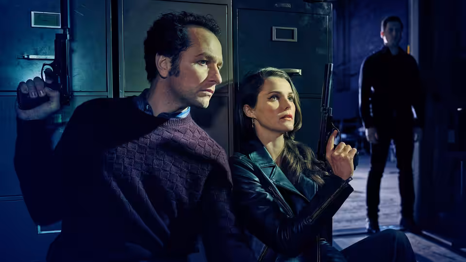 Philip Jennings (Matthew Rhys) and Elizabeth Jennings (Keri Russell) holding guns near metal lockers