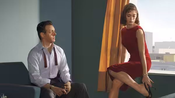 A man in a white shirt sits facing a woman in a red dress on a windowsill