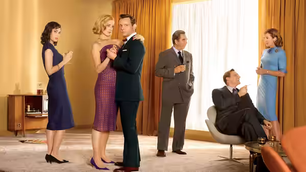 A man and woman dance while others watch in a mid-century furnished living room