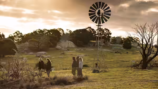 Four people standing in grass near a windmill under a cloudy sky