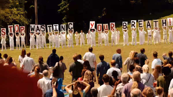Crowd in white holding letters spelling Stop Wasting Your Breath in a field