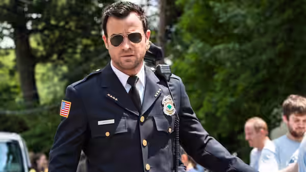 Kevin Garvey (Justin Theroux) in police uniform standing outdoors with trees behind