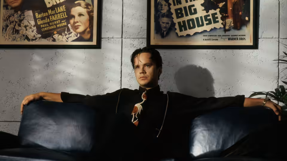 Griffin Mill (Tim Robbins) reclining on a blue couch beneath movie posters