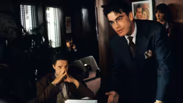 A suited man standing over another man seated in an office