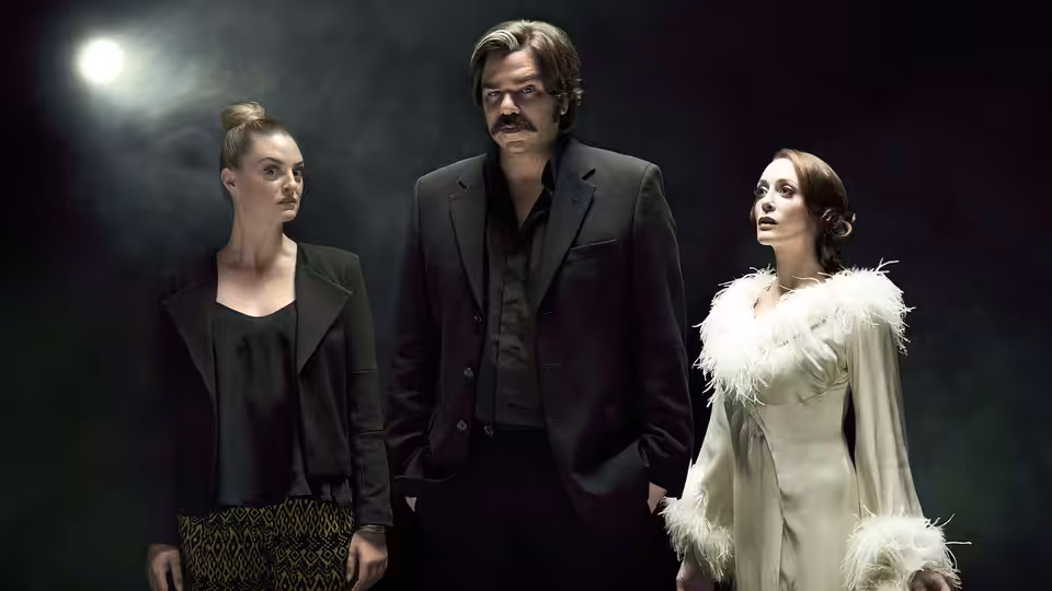 Steven Toast (Matt Berry) standing between two women under a spotlight