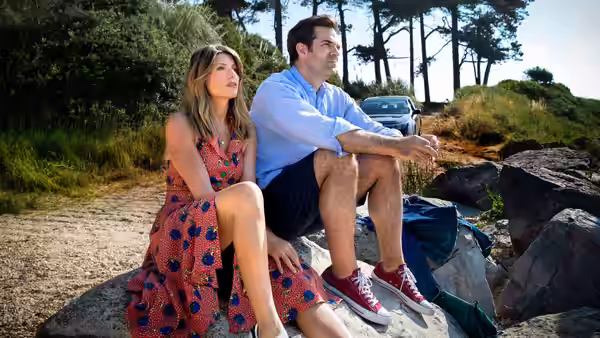 Sharon (Sharon Horgan) and Rob (Rob Delaney) seated on rocks outdoors