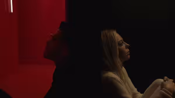 A man and woman sit side by side in a red-lit room
