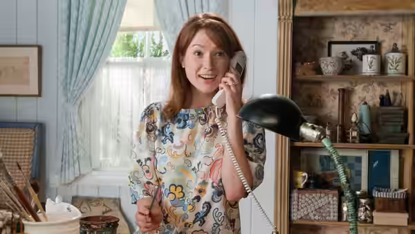 Kimmy Schmidt (Ellie Kemper) smiling while talking on the phone in a craft room