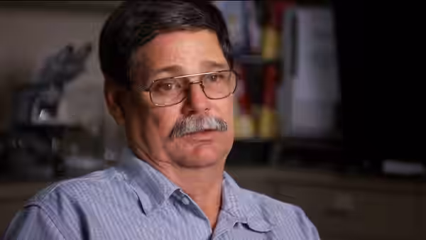 Man with glasses and mustache seated indoors in an office setting
