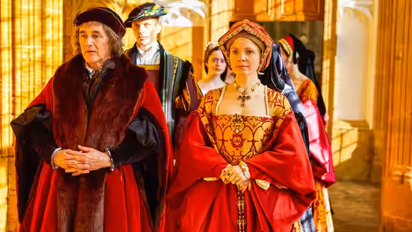 Cardinal Wolsey (Jonathan Pryce) stands with Anne Boleyn (Claire Foy) in a hall