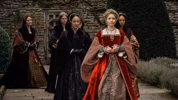 Anne Boleyn (Claire Foy) walks ahead of ladies in black gowns outdoors