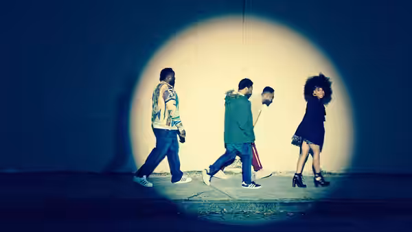 Four people walking in single file under a bright spotlight