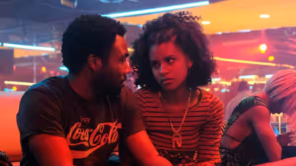 A man and woman facing each other in a red lit bar