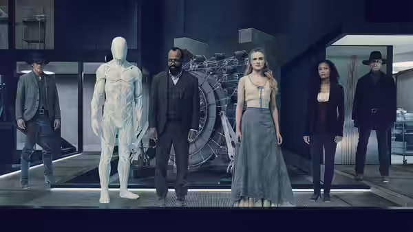 A blonde woman in a gray dress stands in a high-tech lab beside a white humanoid figure and suited men