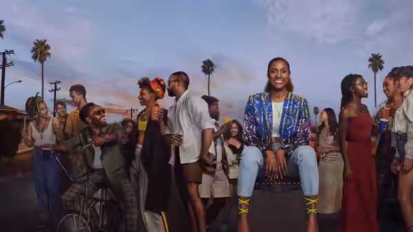 Issa Dee (Issa Rae) smiles seated on a chair among friends on a street