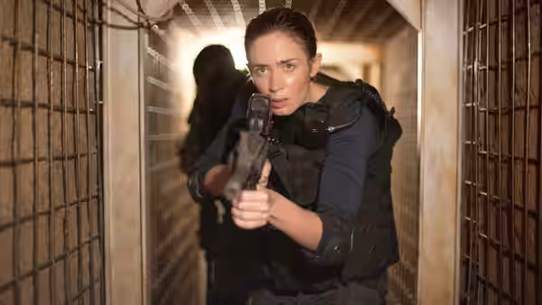 Kate Macer (Emily Blunt) aiming a handgun in a barred corridor