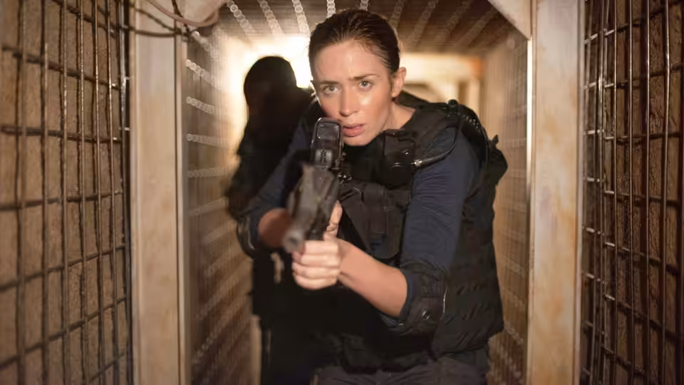 Kate Macer (Emily Blunt) aiming a handgun in a barred corridor