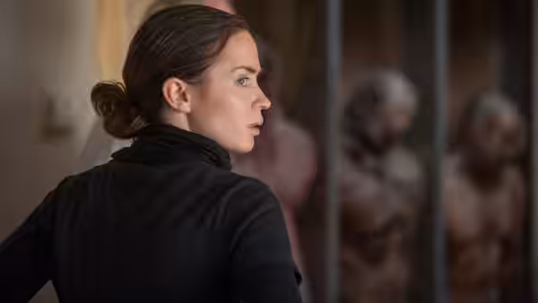 Kate Macer (Emily Blunt) looking toward prisoners behind metal bars