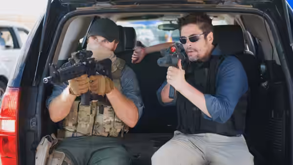 Two armed men with guns positioned inside the back of a vehicle