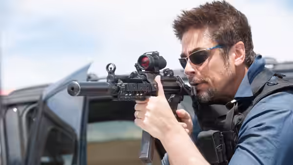 Man in sunglasses aiming a rifle from behind an open vehicle door