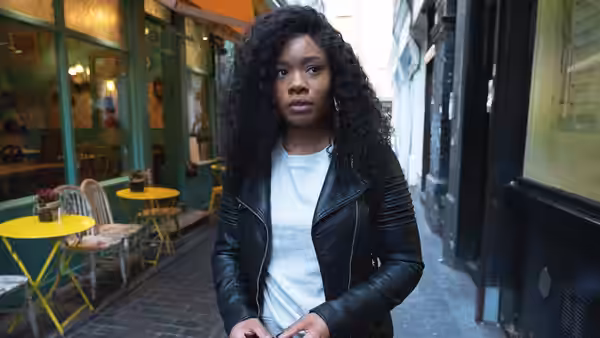 Woman with curly black hair standing on a narrow city street