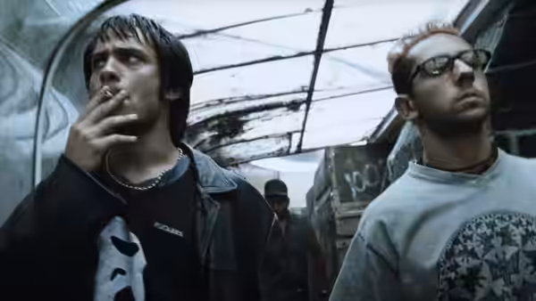 Two men standing in a dimly lit industrial space one smoking