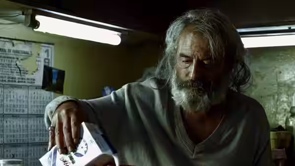 El Chivo (Emilio Echevarría) examining papers in a cluttered workspace