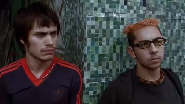 Two young men standing side by side against a green tiled wall