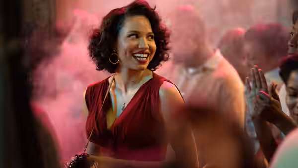 Letitia Lewis (Jurnee Smollett) smiling in a red dress at a crowded party