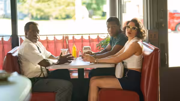 Letitia Lewis (Jurnee Smollett) seated with two men in a diner booth