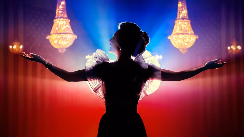 Woman in black dress with arms outstretched on a theater stage