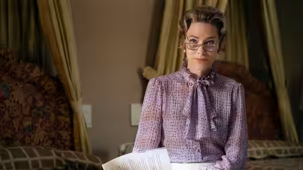 Woman with glasses holding papers while seated on a bed