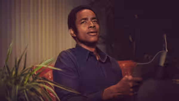 Man in blue shirt reading papers while seated on a red couch