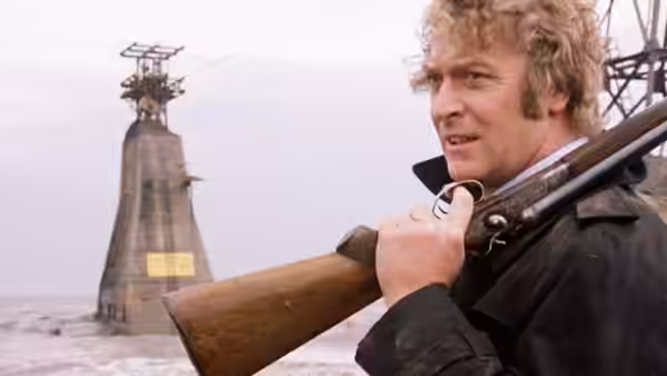 Jack Carter (Michael Caine) carrying a shotgun past a sea tower