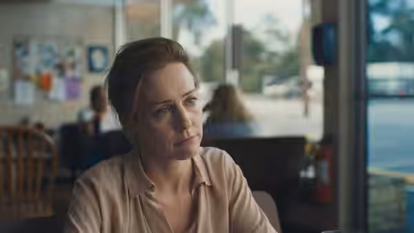 a woman in a beige shirt sits in a diner looking to the side