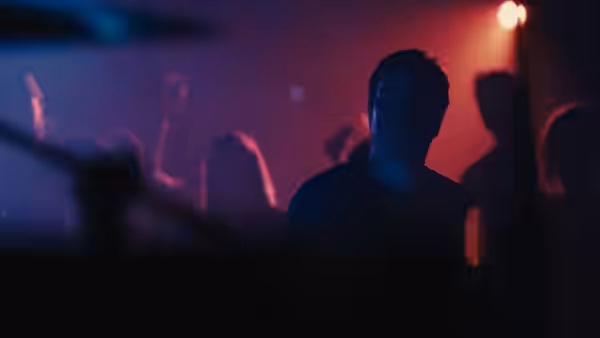 a man stands in a crowded nightclub lit with purple and red lights
