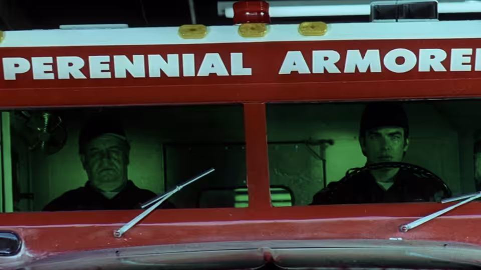 Two men in uniform sit inside the cab of a red armored truck