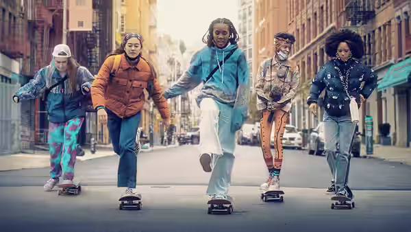 Five young women on skateboards linked together on a city street